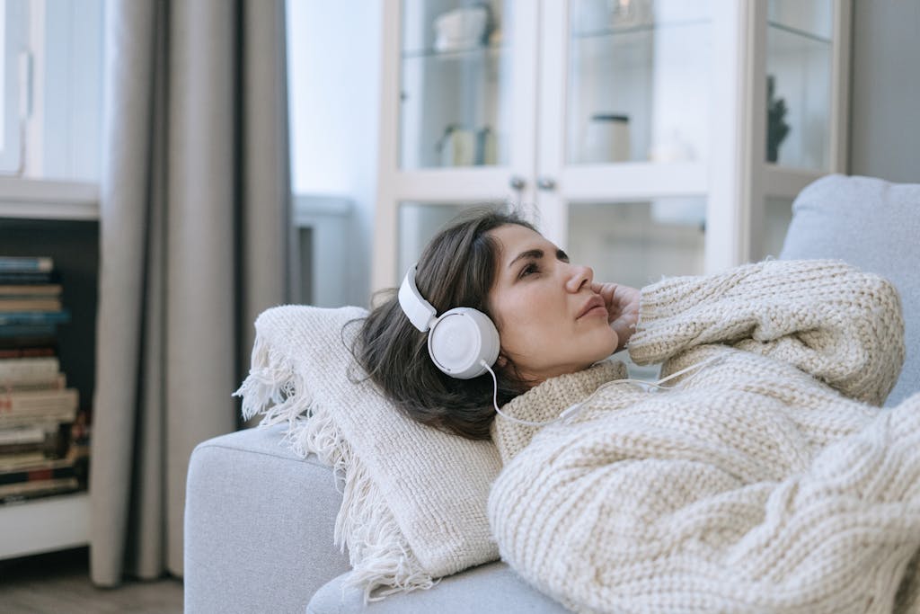 A Woman in a Knitted Sweater Listening to Music while Lying Down on a Couch