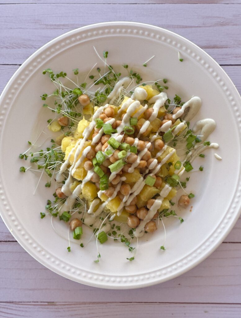 An appetizing plant-based platter: golden potatoes, spicy chickpeas on a bed of sprouts, garnished with green onions and vegan ranch sauce.