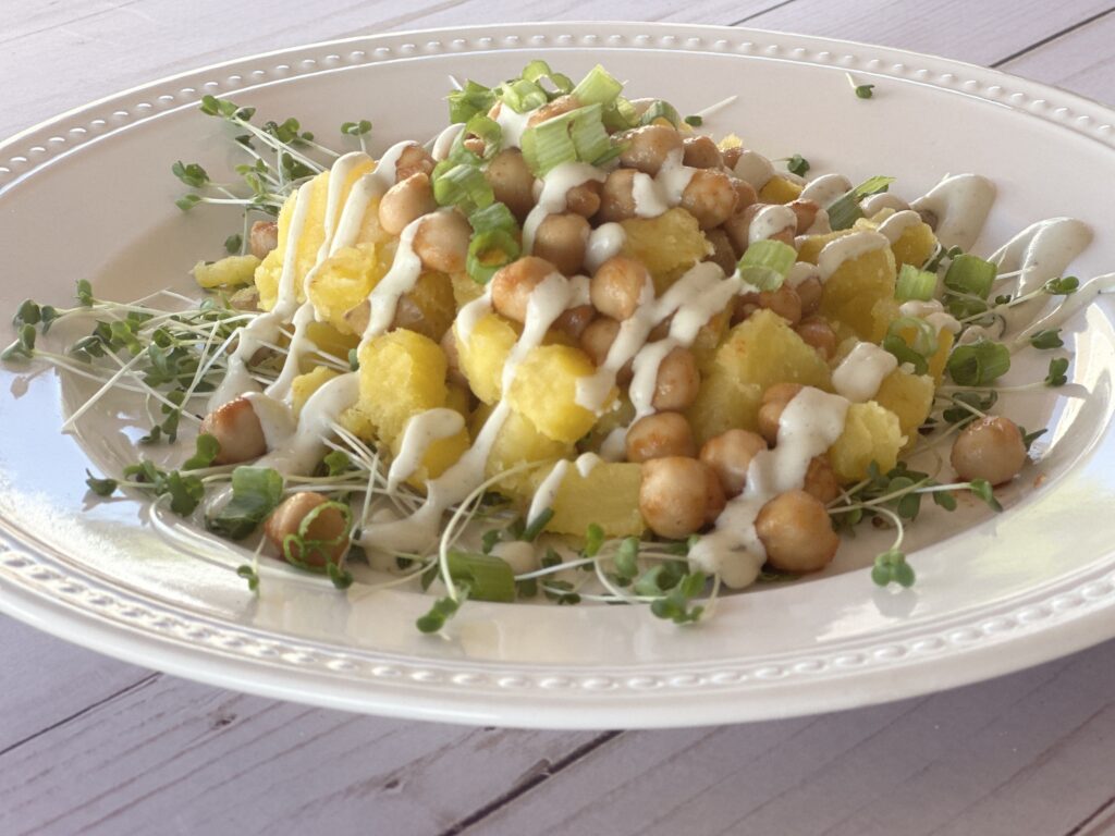 A healthy and flavorful plate of roasted potatoes, botana-flavored chickpeas, and fresh sprouts, topped with green onions and a creamy vegan ranch drizzle.